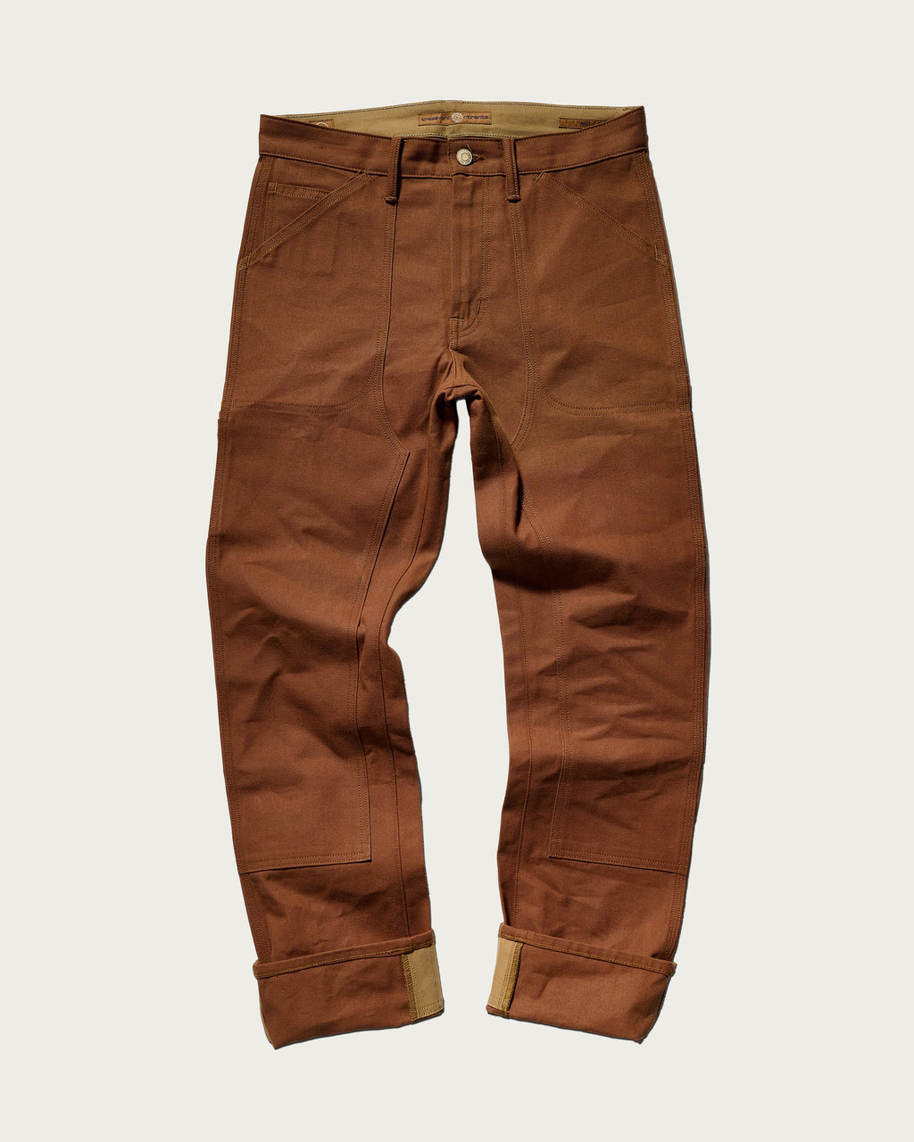 The Sid Pant in Hide Raw by T7C The Seven Continents features visible stitching, large front pockets, and rolled cuffs—crafted for classic workwear style and shown laid flat on a plain white background.