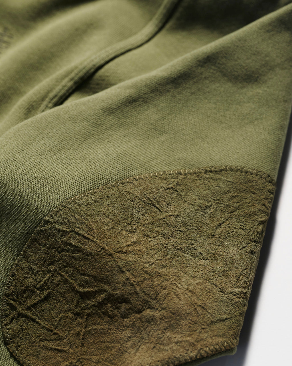 Close-up of olive green fabric with a textured, darker green suede elbow patch—an elevated detail on the relaxed fit Camden Hoodie in Olive by T7C The Seven Continents.
