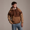 A man wears the T7C The Seven Continents Hunter Hoodie in Terra over a white collared shirt and blue jeans, standing against a plain background with one hand in his pocket, looking to his left.