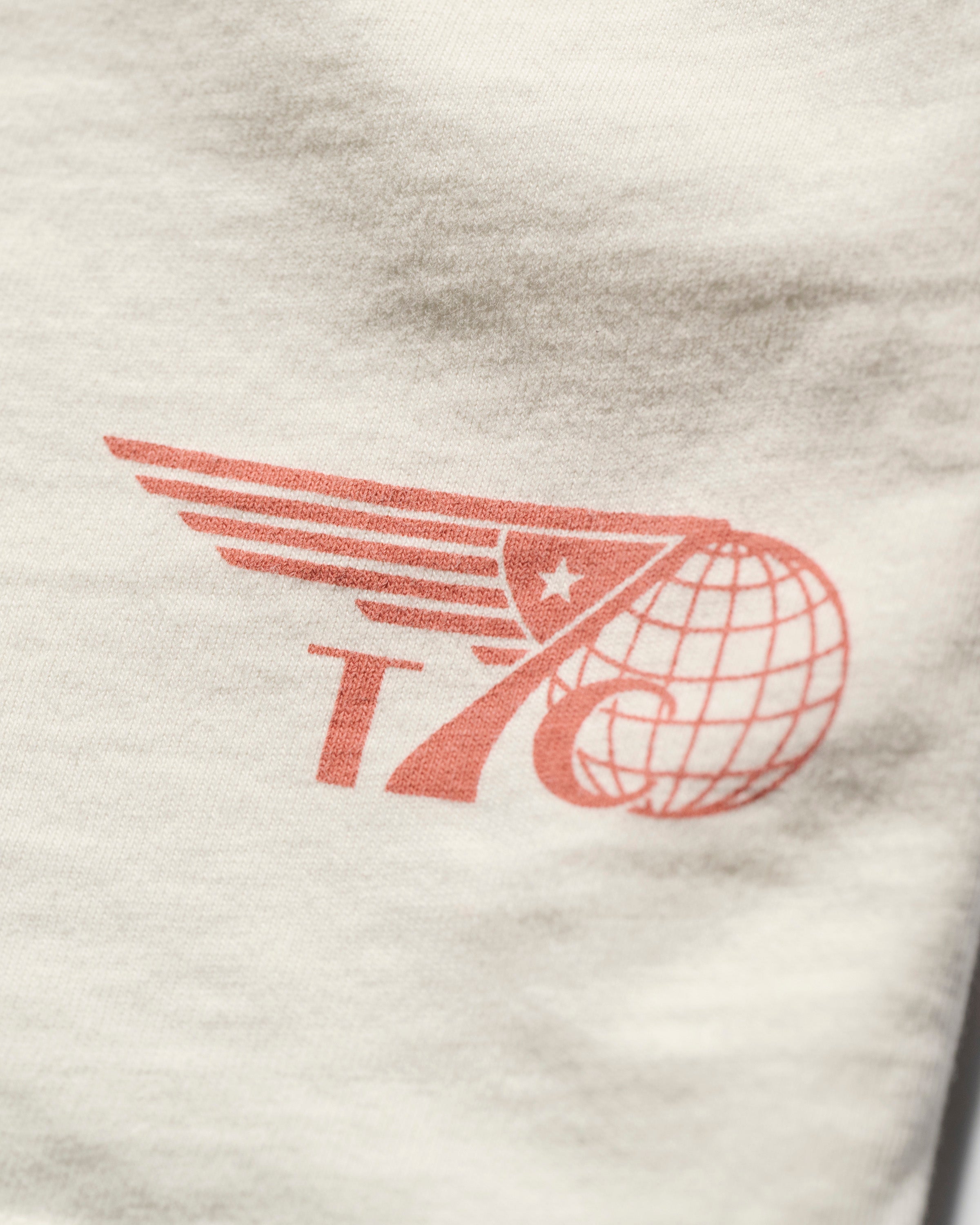 The T7C THE KNOXS TEE WITH ICON PRINT features a red graphic with the number 76, a wing, globe, and star on white fabric, with the design printed in the corner.