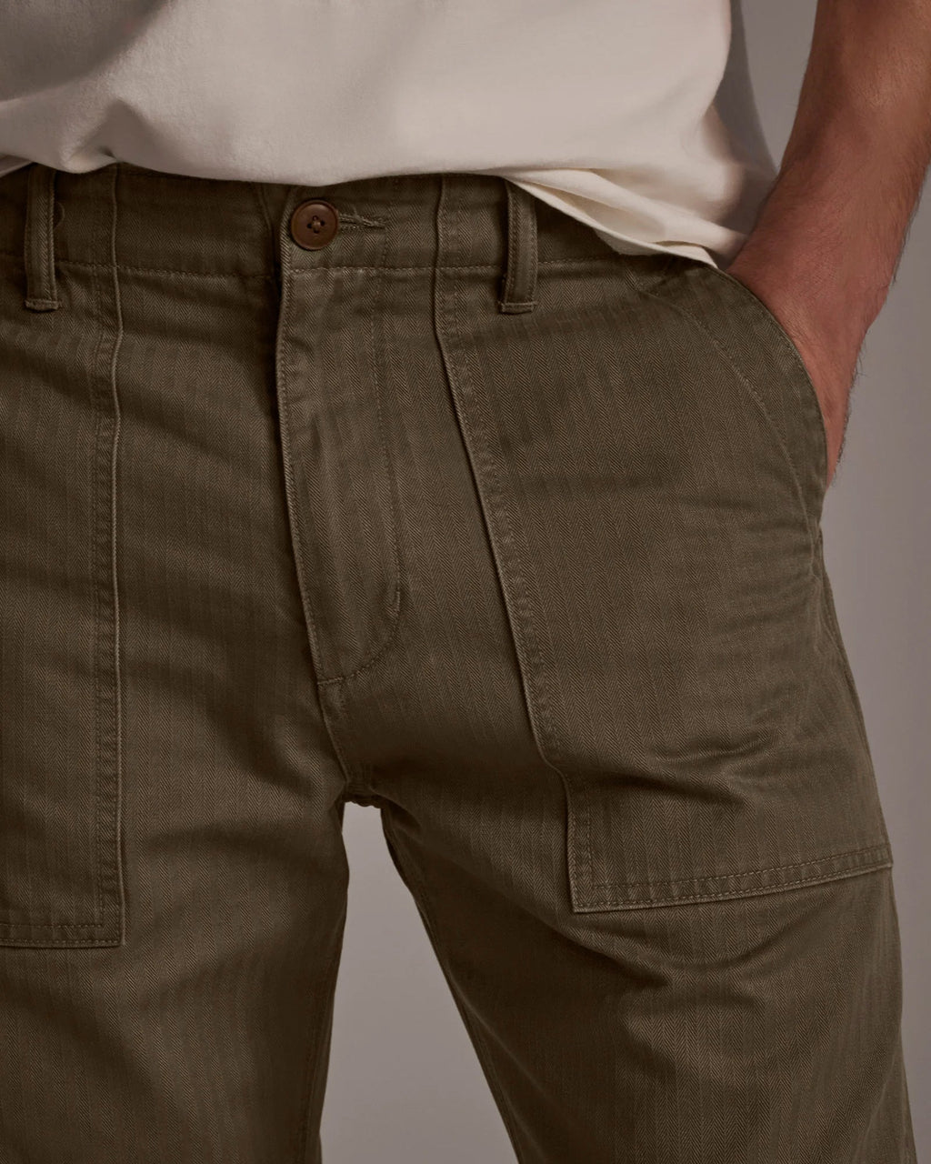 Wearing T7C’s The Liam Military Pant in Olive Drab—relaxed-fit with a button closure and front pockets—paired with a white shirt partially tucked in, one hand casually in the pocket.