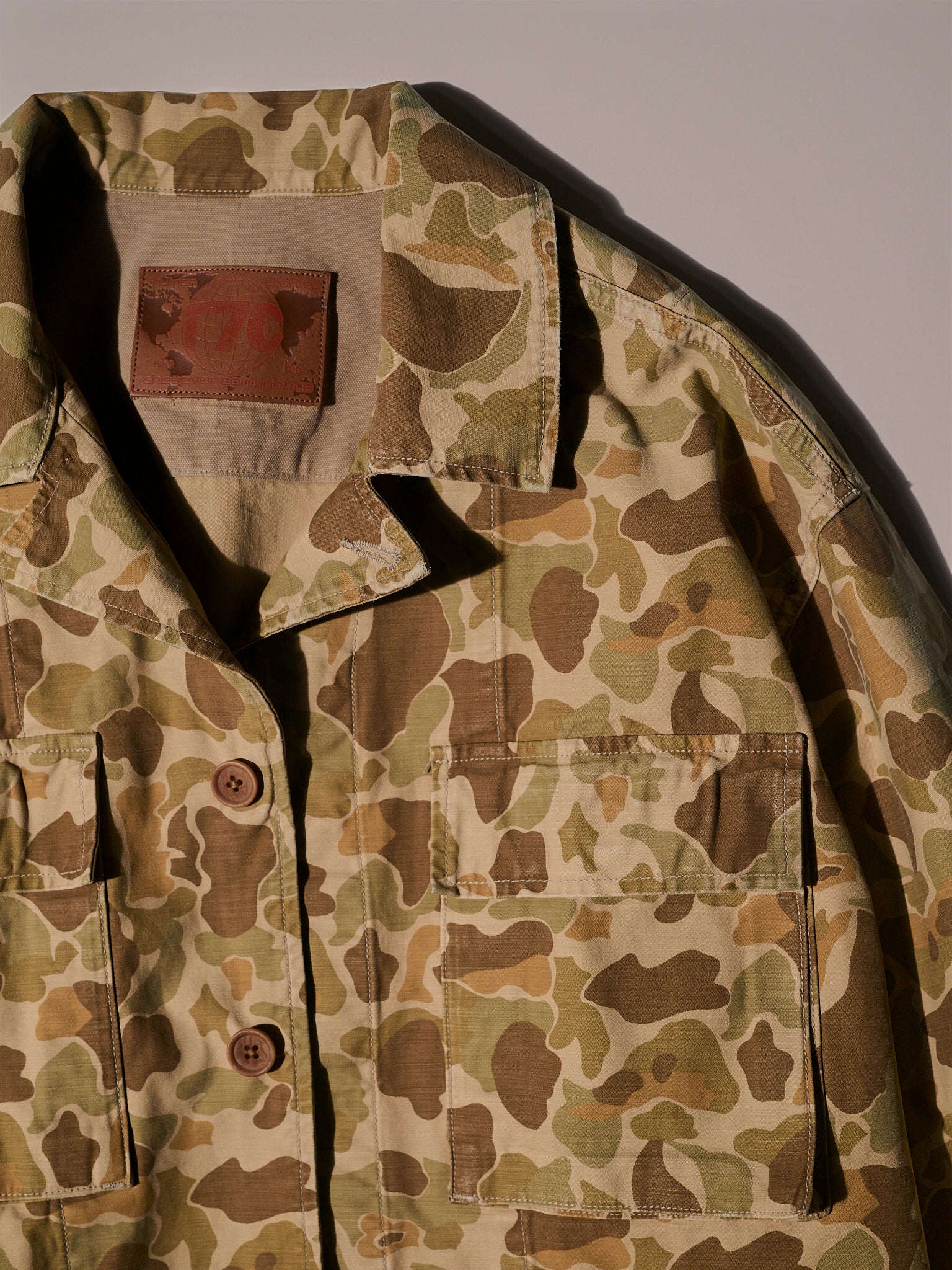 The Ryan Jacket in Camouflage by T7C The Seven Continents is a relaxed-fit cotton-back satin overshirt featuring light brown, green, and tan camo, brown buttons, and two front chest pockets, shown flat under soft lighting.