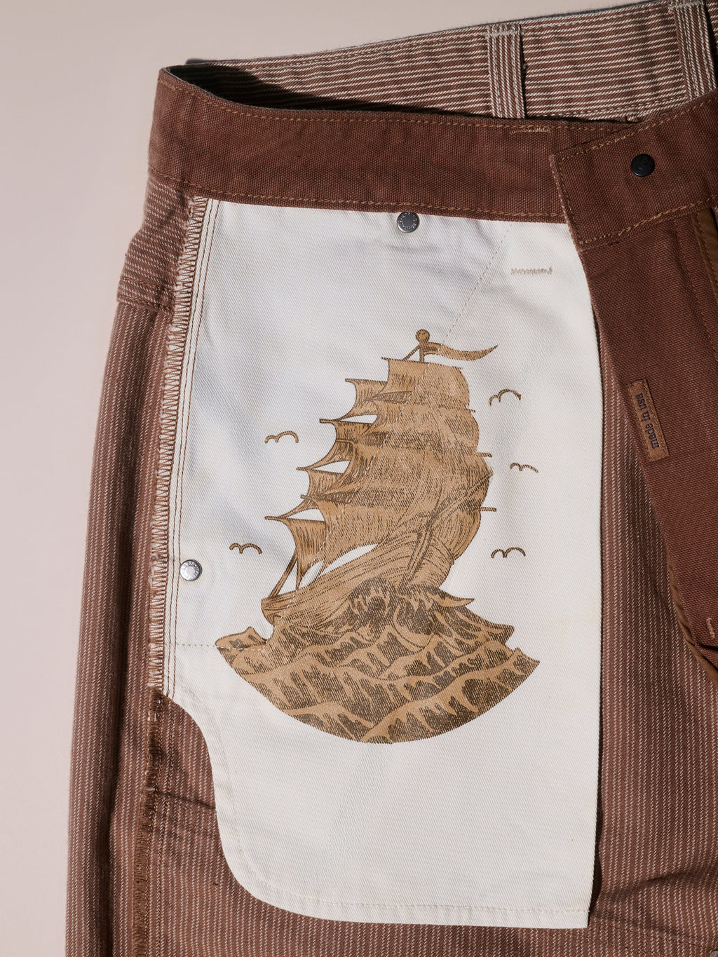 Close-up of the inside pocket of T7Cs The Fred Pant in Camel Stripe, featuring a printed illustration of a tall sailing ship on waves with birds flying above.