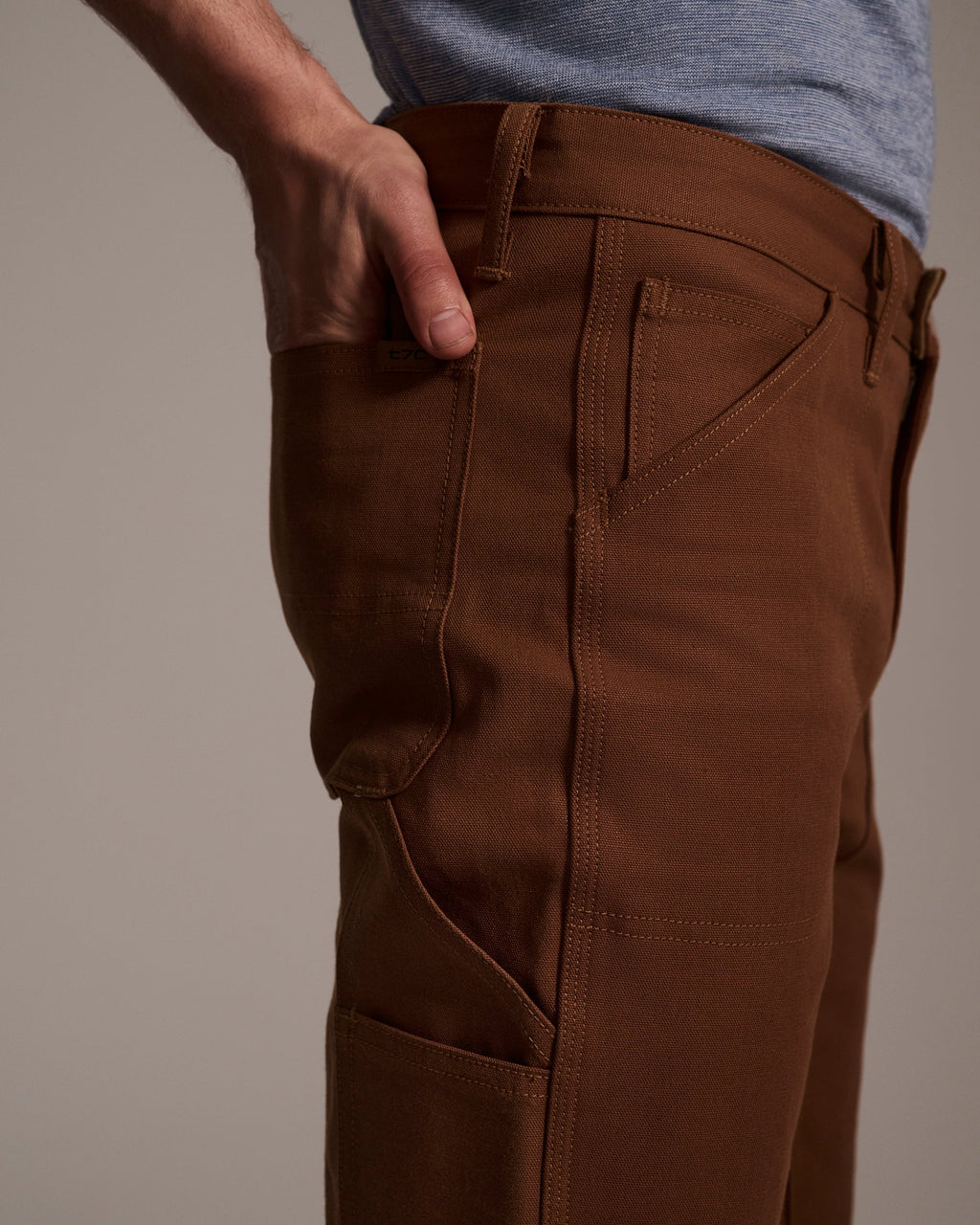 Someone stands with one hand in their pocket, wearing T7C The Seven Continents’ The Sid Pant in Hide Raw, shown from the waist down against a neutral background.