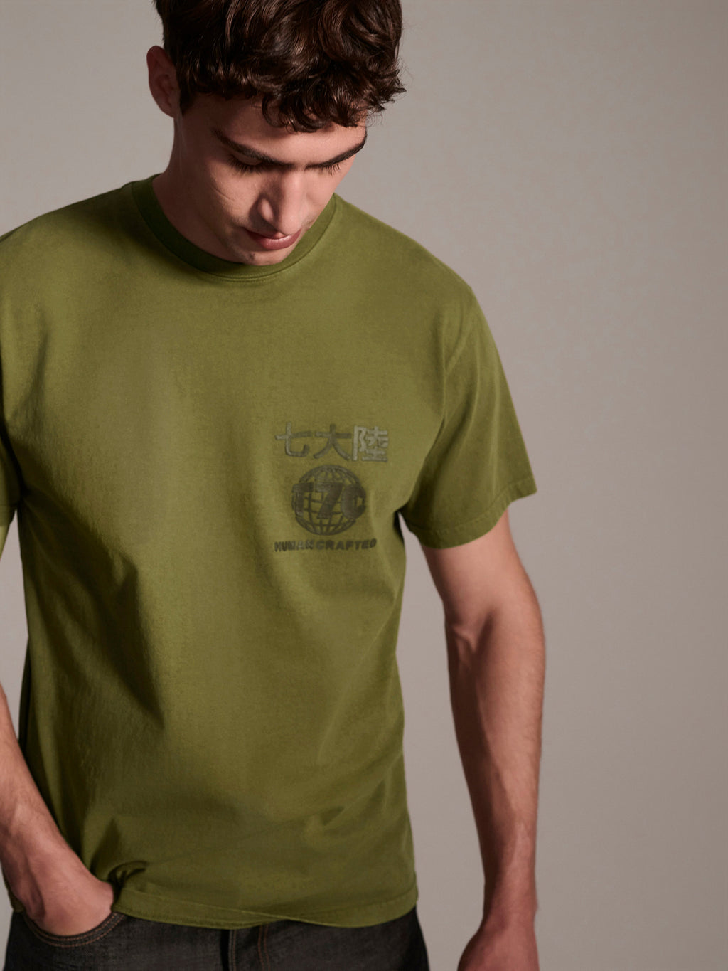A male model wearing a olive t-shirt with a logo detail