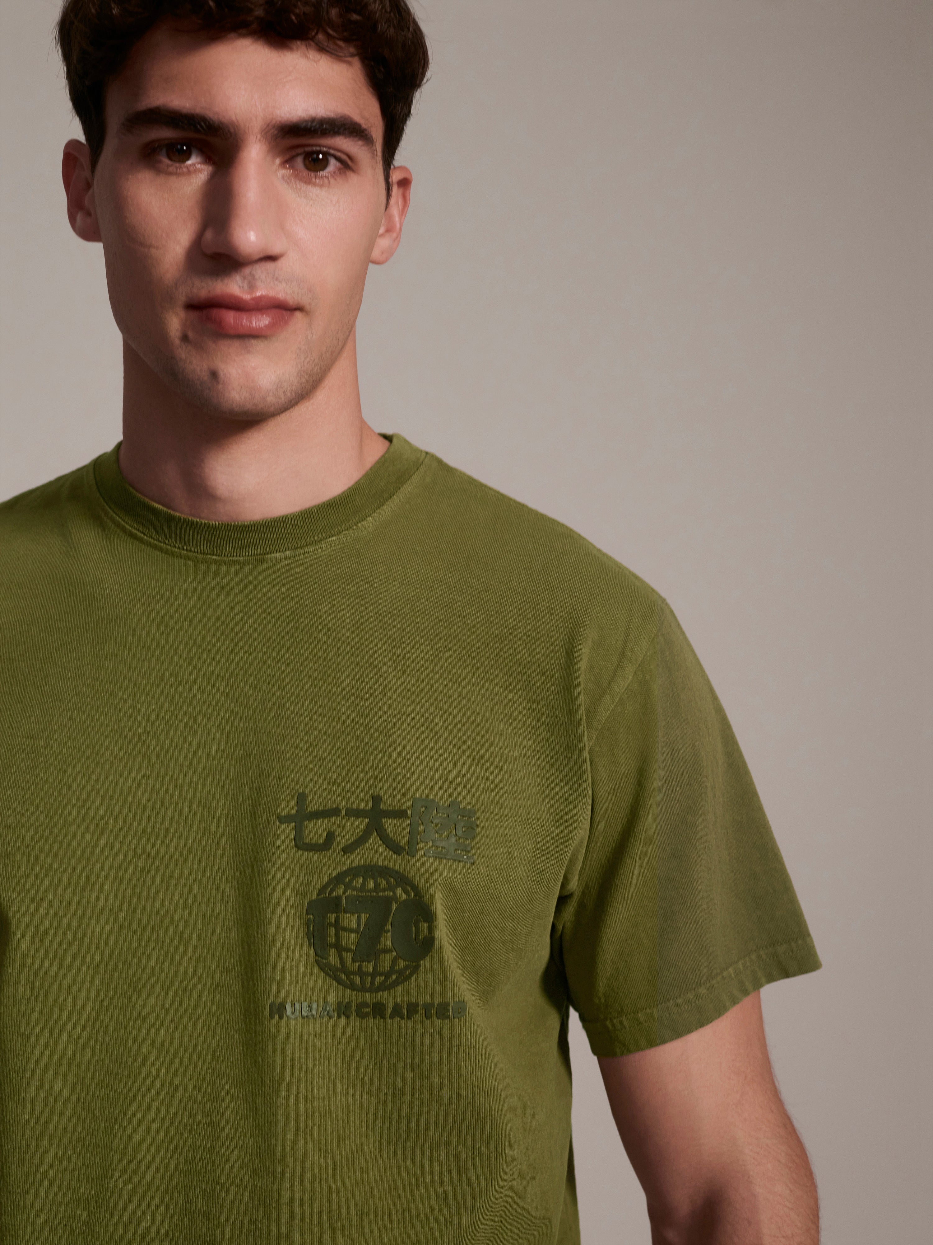 A detail image of a male model wearing a olive t-shirt with a logo detail